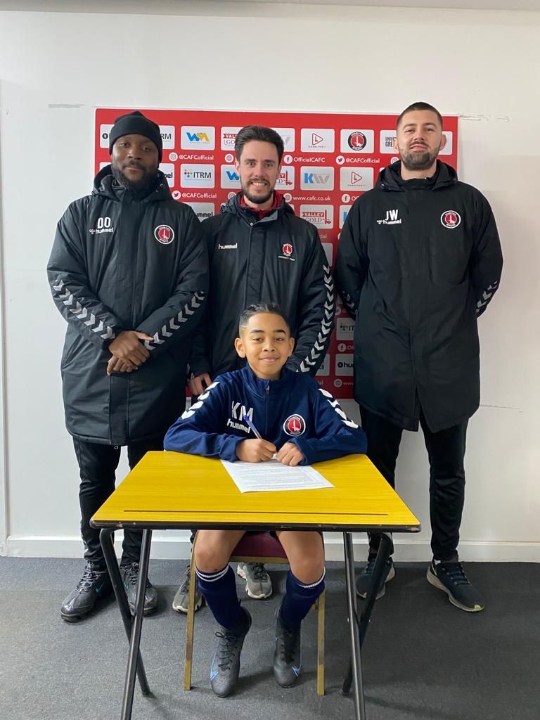 Kyan May at a table signing his contract with CACT and CAFC staff