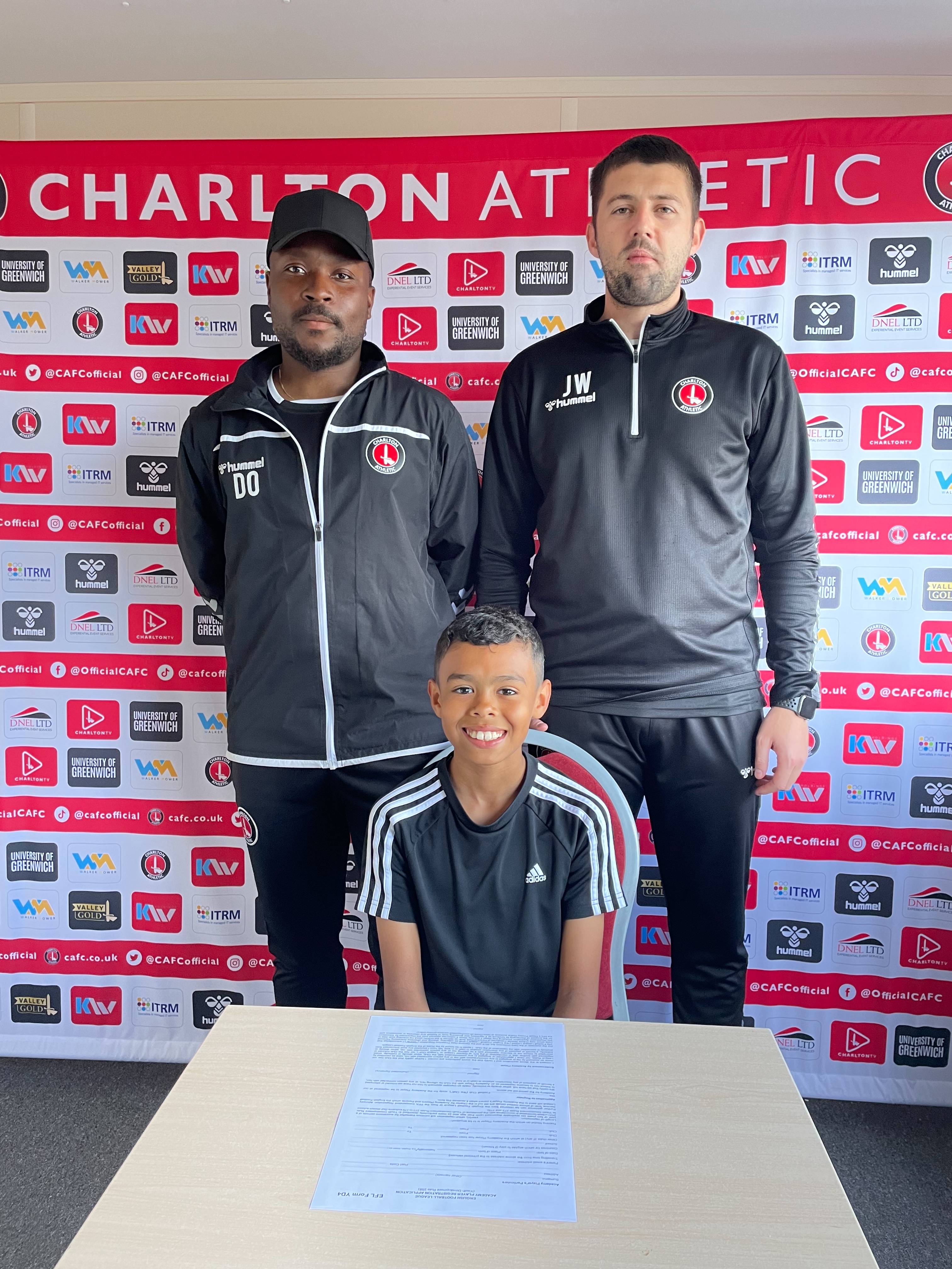 Jake Maloney signing his contract at a small table alongside CAFC Academy staff