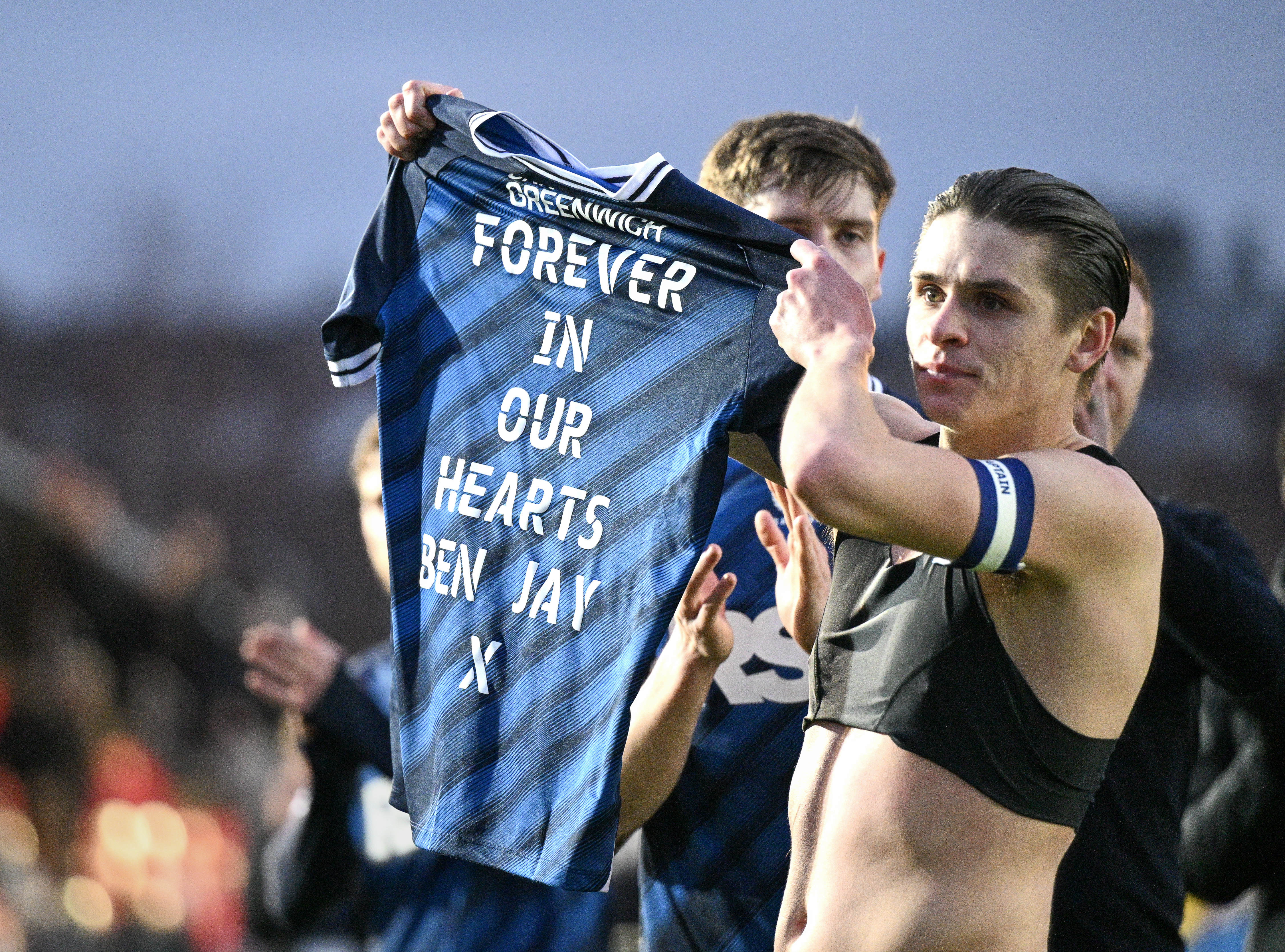 Dobson holds up shirt saying "Forever in our hearts Ben Jay x"
