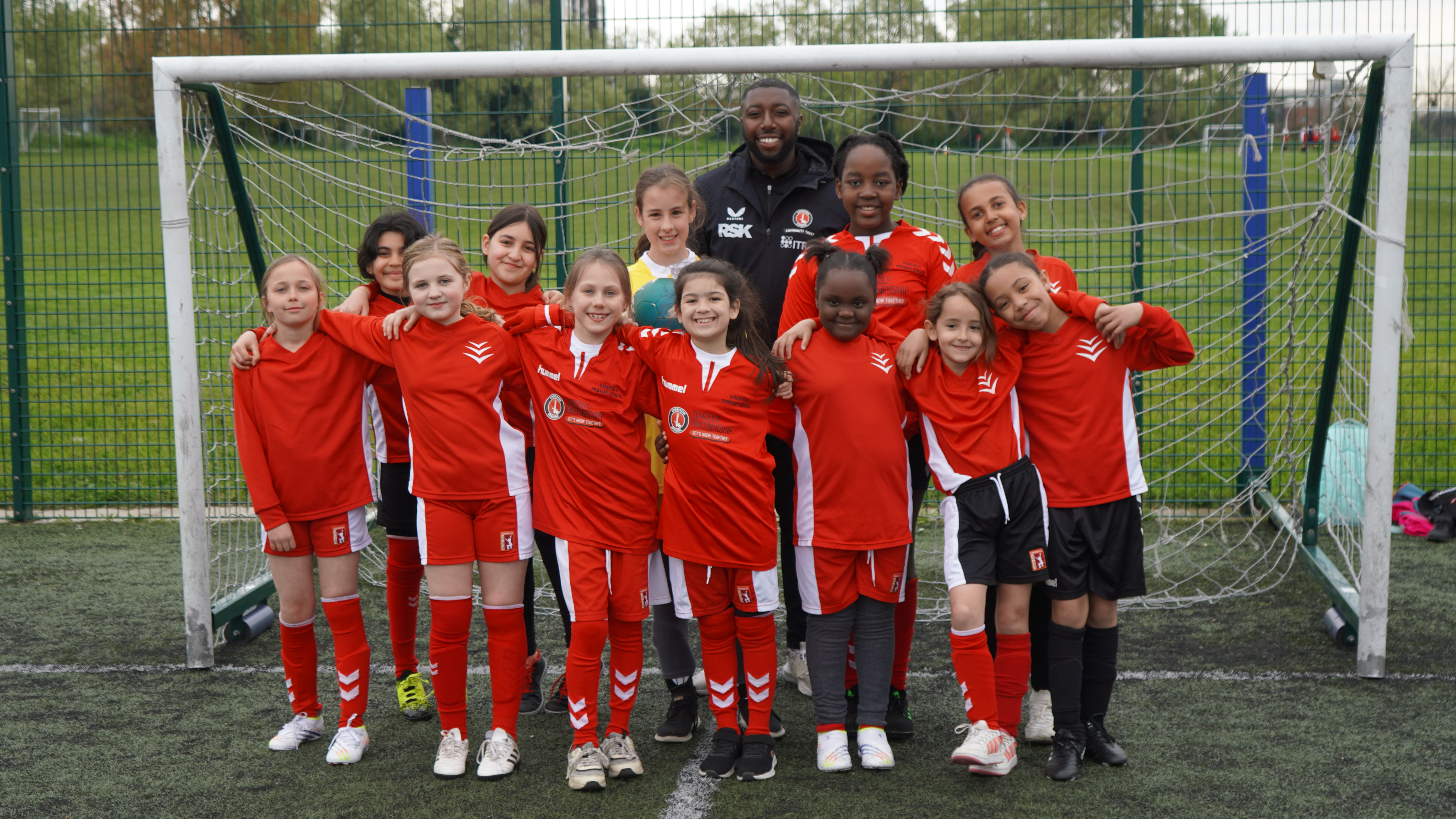 Girls football team in Charlton kits with CACT Coach Ivan posing inside a goal