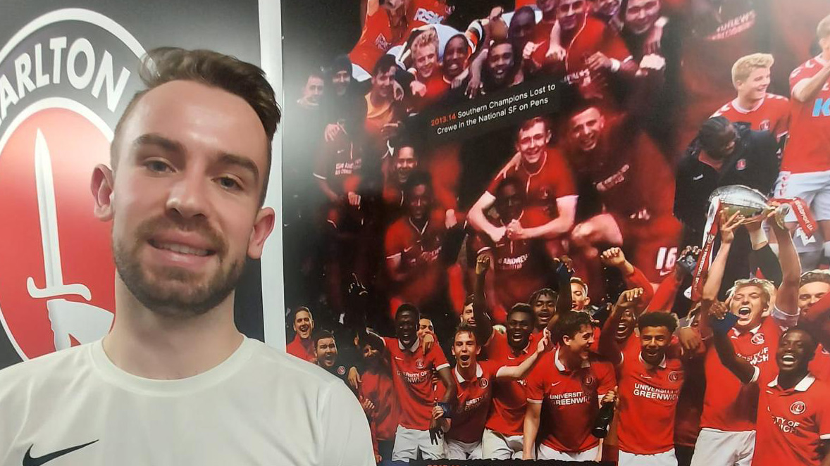Alex Willis standing in front of a backdrop of academy players.