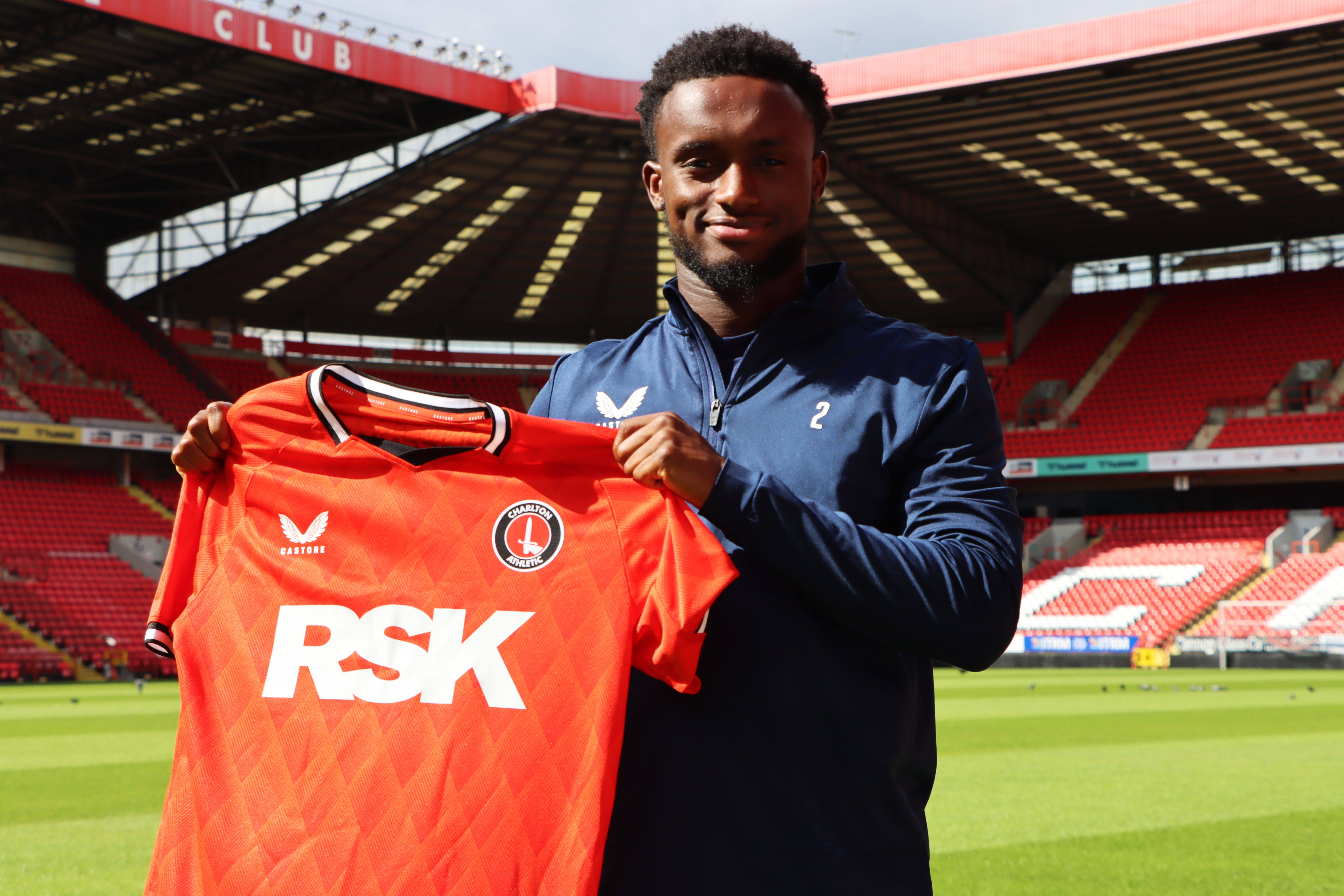Steven Sessegnon holds up Charlton's new 2022/23 home shirt while on the pitch at The Valley