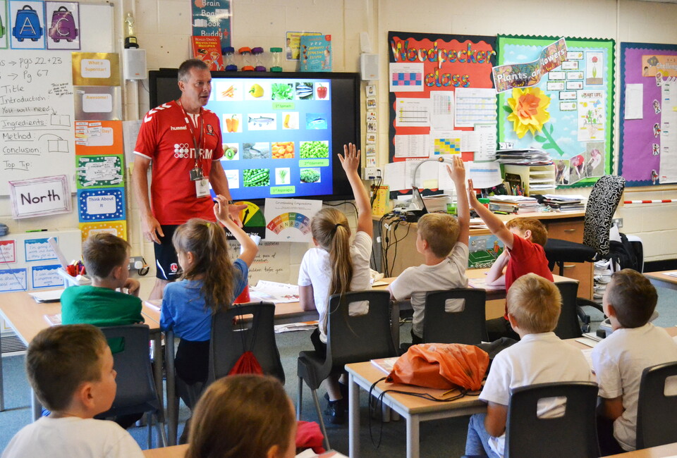 CACT coach at the front of a classroom of kids with their hands up