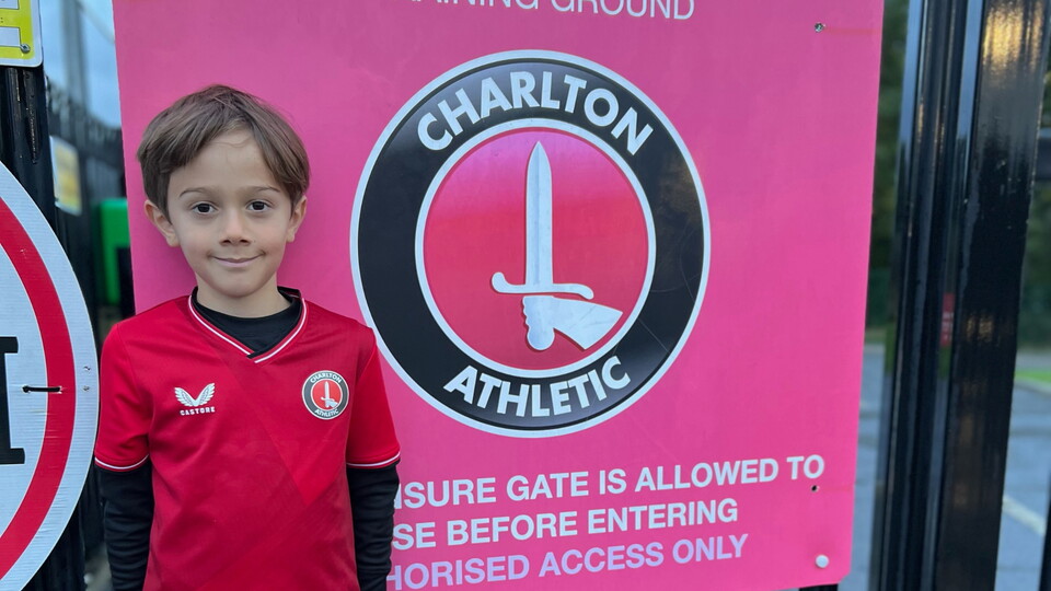 Oli Fairley in Charlton Athletic kit stood next to a Charlton Athletic logo.