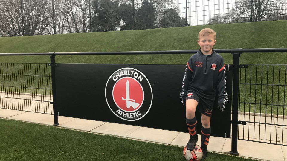 Harry Markley with a football under his foot next to a Charlton Athletic logo