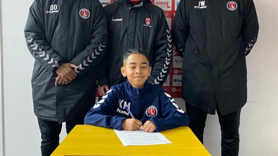 Kyan May at a table signing his contract with CACT and CAFC staff