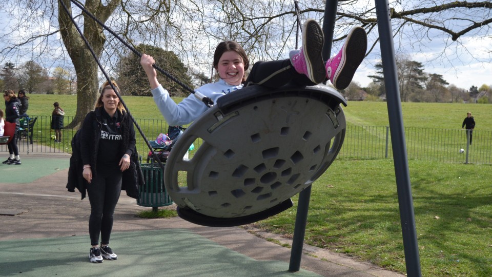 Image of a Short Breaks participant being pushed on a swing by a CACT staff member