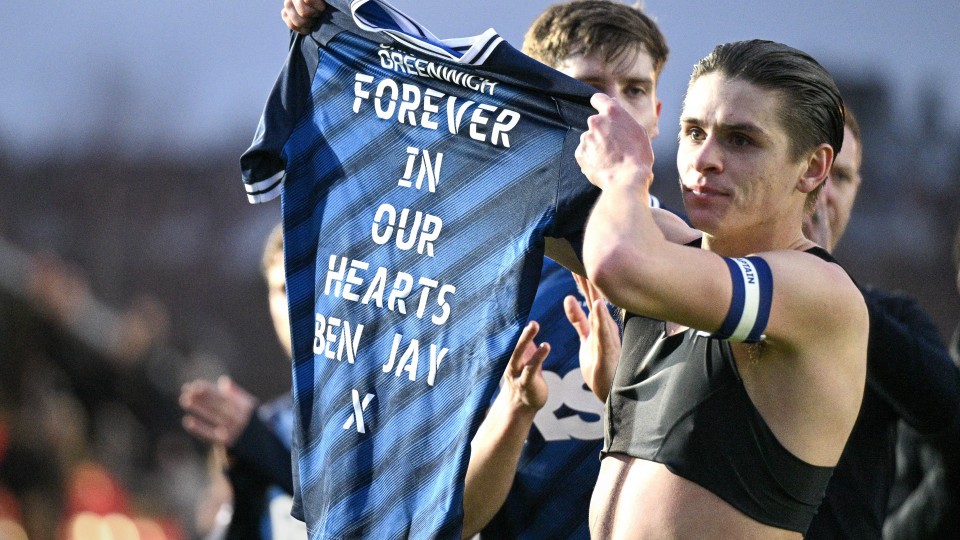 Dobson holds up shirt saying "Forever in our hearts Ben Jay x"